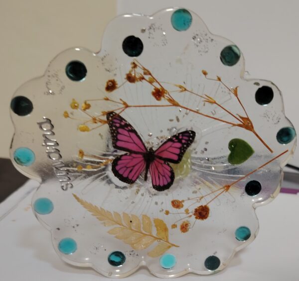 Handmade transparent resin coaster with dried flowers, pink butterfly, gold flakes, and scalloped edges — artistic and nature-inspired decor piece.